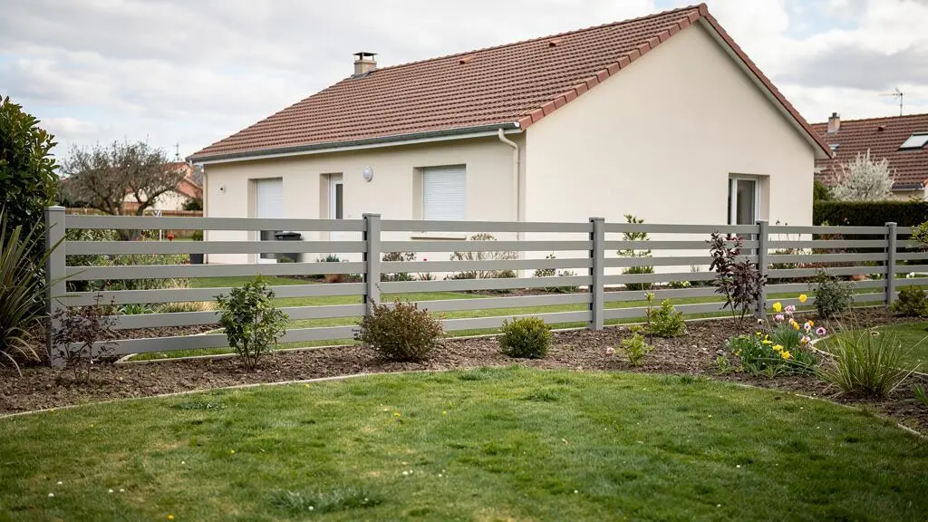 Clôture moderne en aluminium gris installée le long d'un jardin résidentiel français avec pelouse et maison pavillonnaire en arrière-plan
